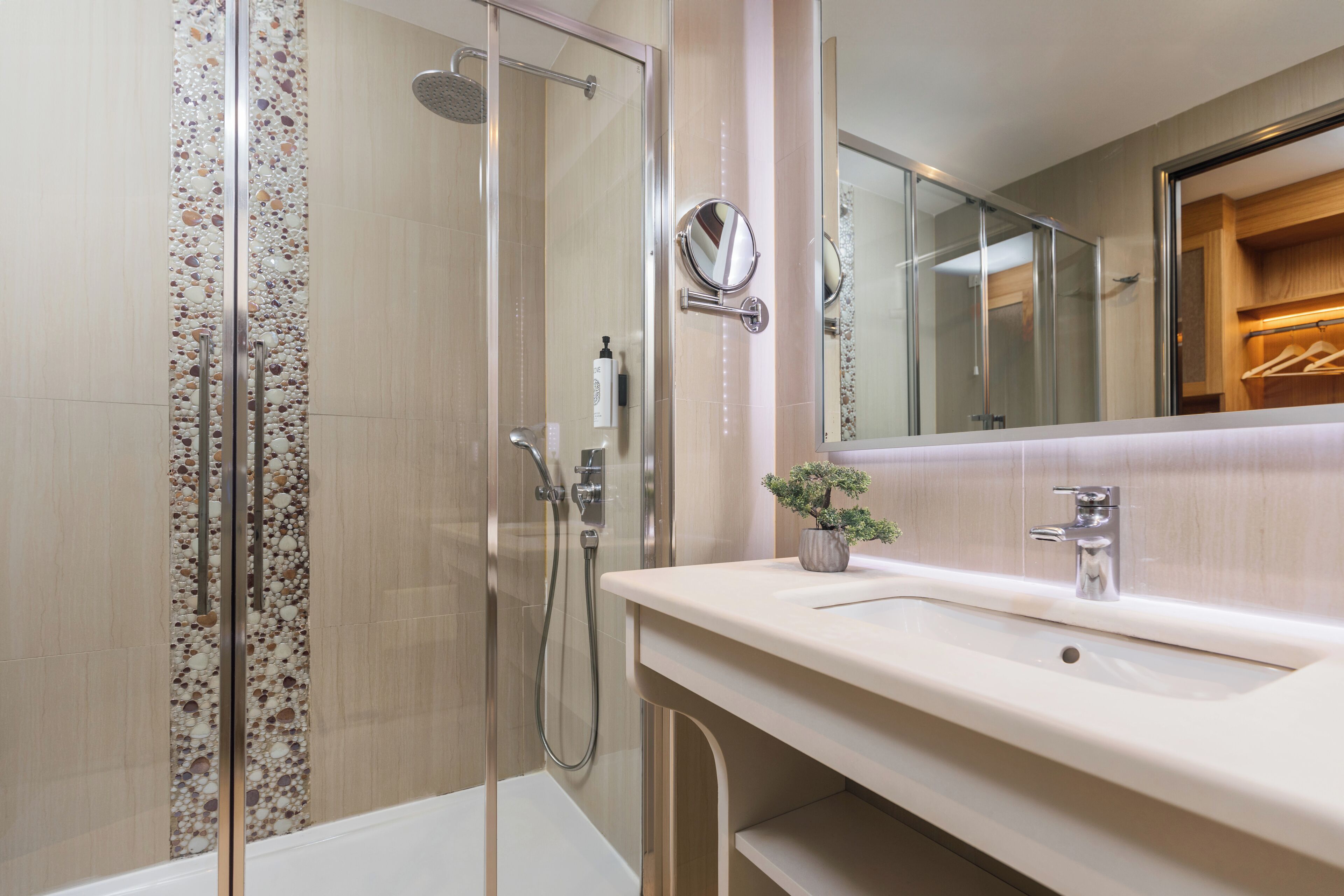 Un bagno moderno con cabina doccia in vetro, lavabo con specchio e una pianta in vaso.