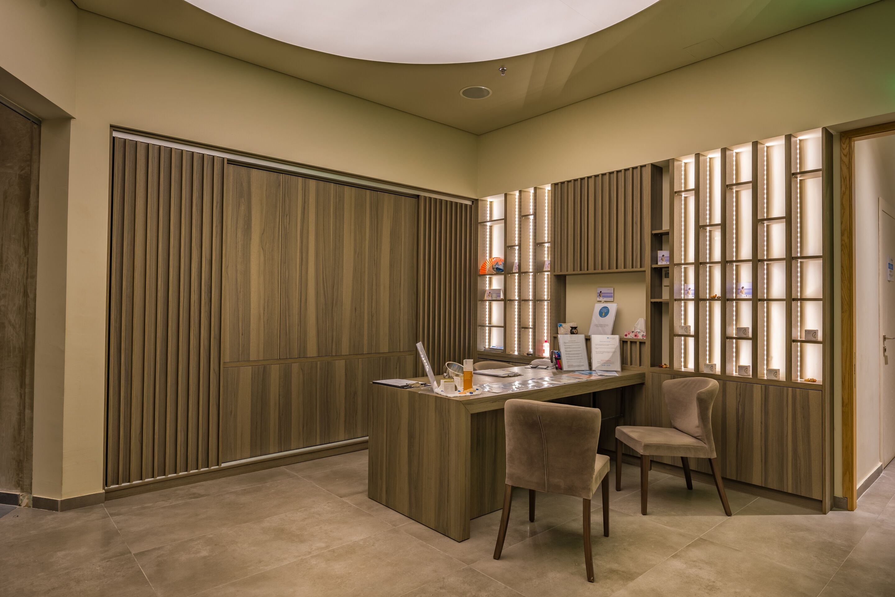 A modern reception area with a wooden panel wall, a reception desk, two chairs, and a wall-mounted display.