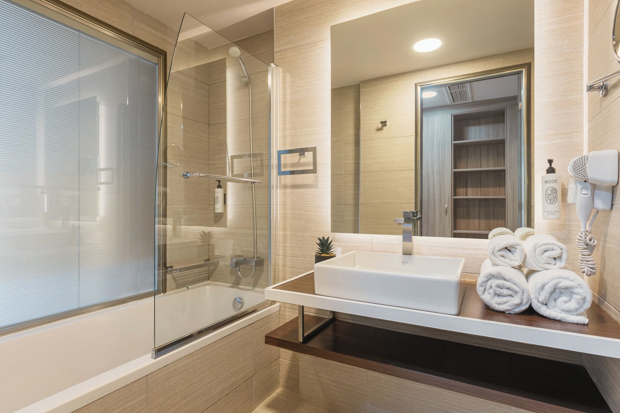 A modern bathroom with a glass-enclosed shower, a white sink, and a mirror reflecting a wooden vanity and a towel rack.