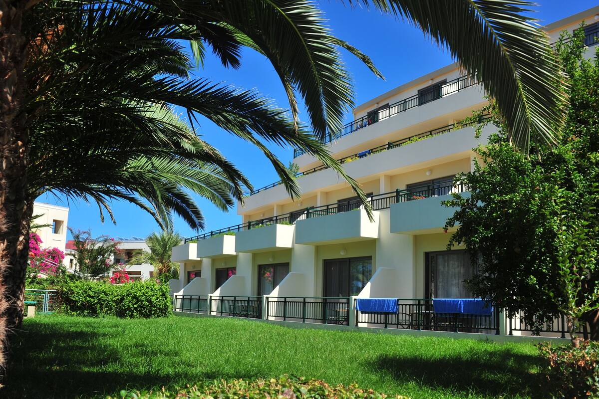 A multi-story hotel with balconies, a well-maintained lawn, and palm trees.