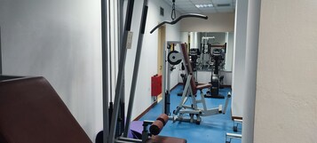 A gym with exercise equipment, a blue floor, and a mirror reflecting the equipment.