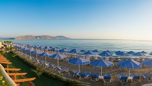 A beach with rows of blue-striped umbrellas and lounge chairs facing the sea. - Hydramis Palace Beach Resort (Apokoronas)