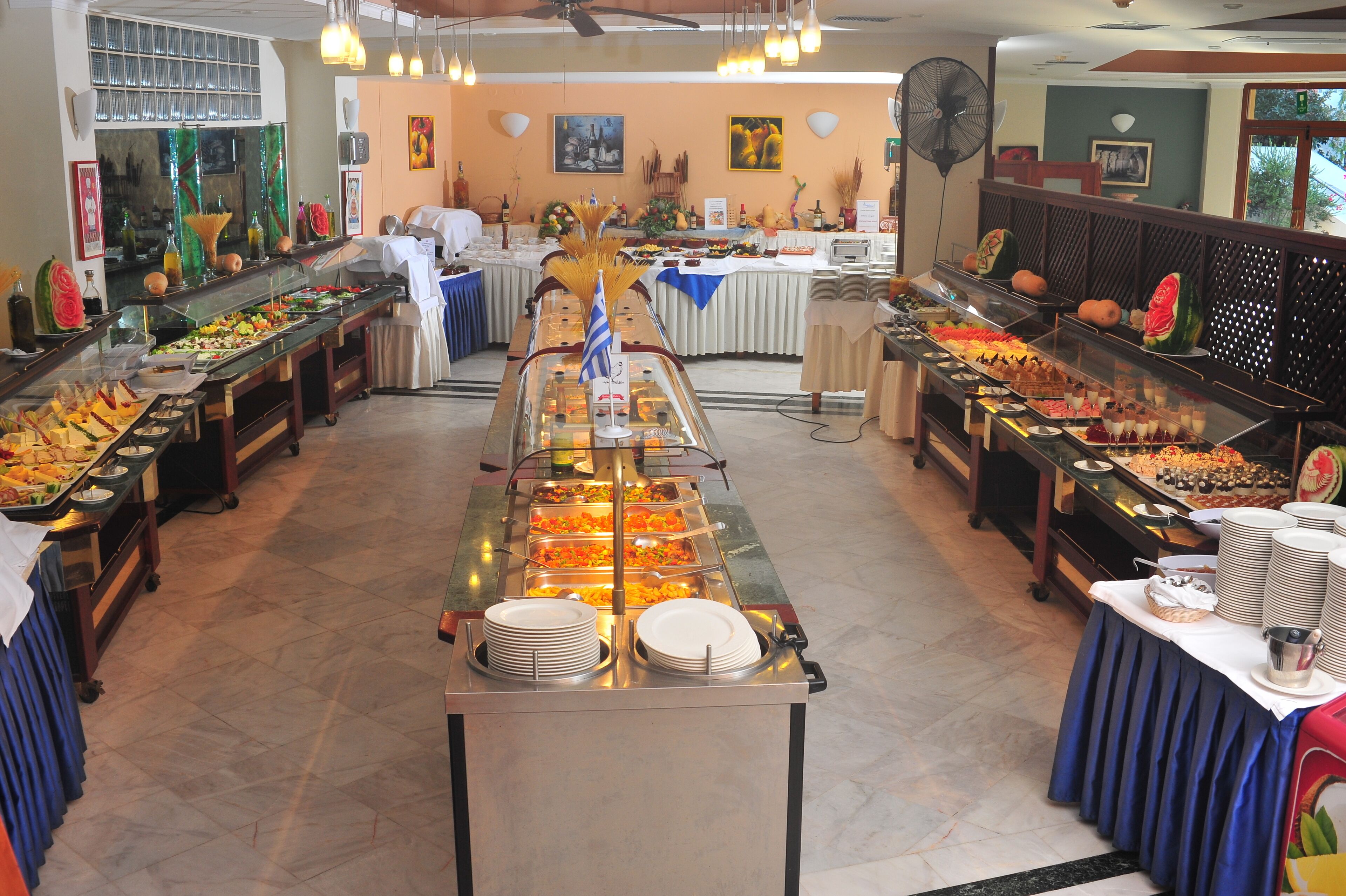 A buffet with various food stations and a fan in the background.