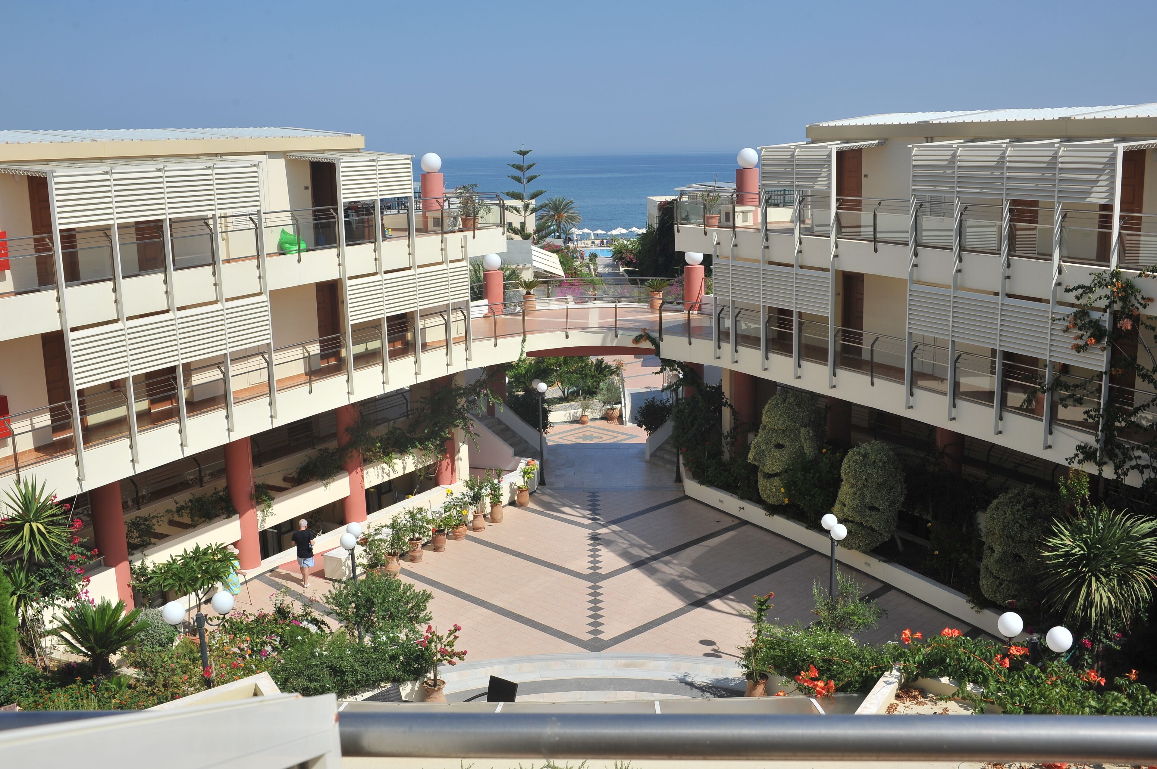 A multi-level hotel with balconies, a central courtyard, and a view of the sea.
