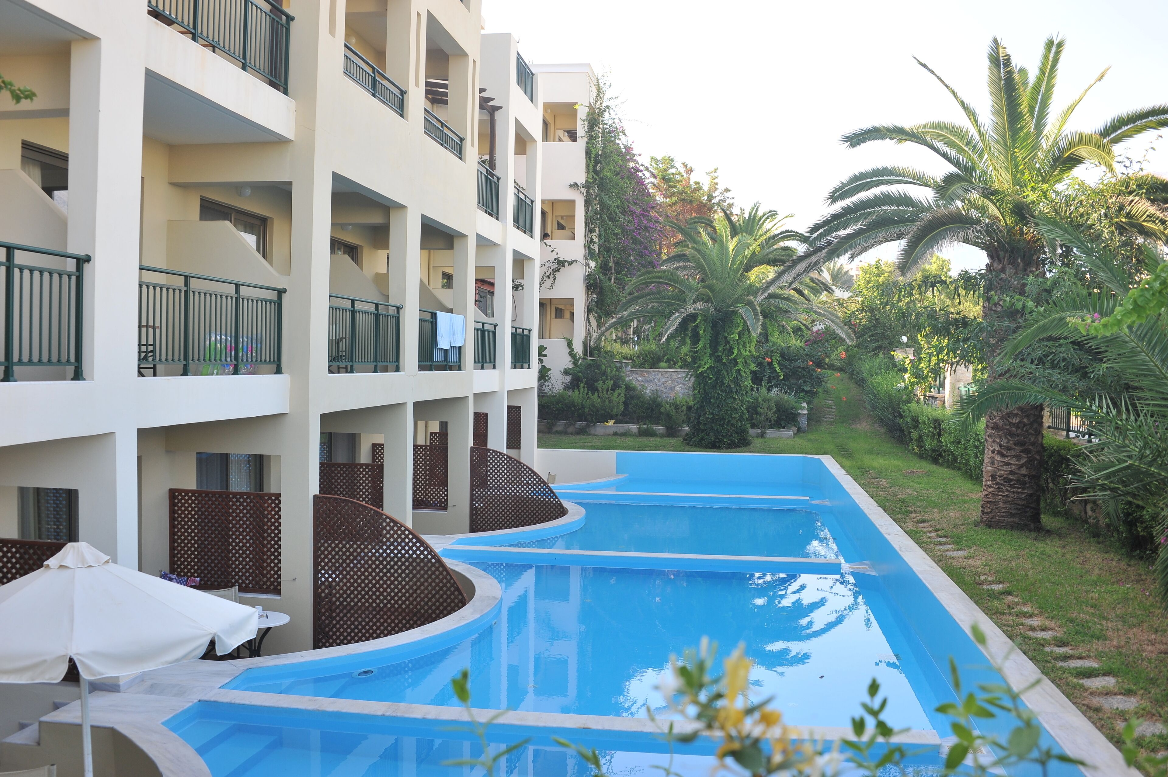 A swimming pool area with a multi-level building, palm trees, and a covered seating area.