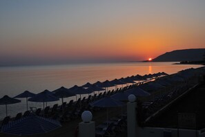 A beach with rows of sun loungers and umbrellas, a sunset in the background, and a calm sea. - Hydramis Palace Beach Resort (Apokoronas)
