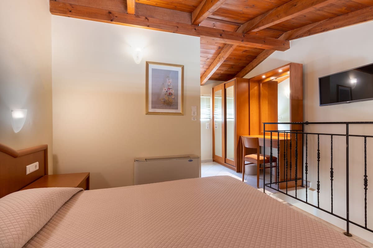 A bedroom with a bed, a radiator, a framed picture on the wall, a TV mounted on the wall, and a wooden staircase leading to another room.