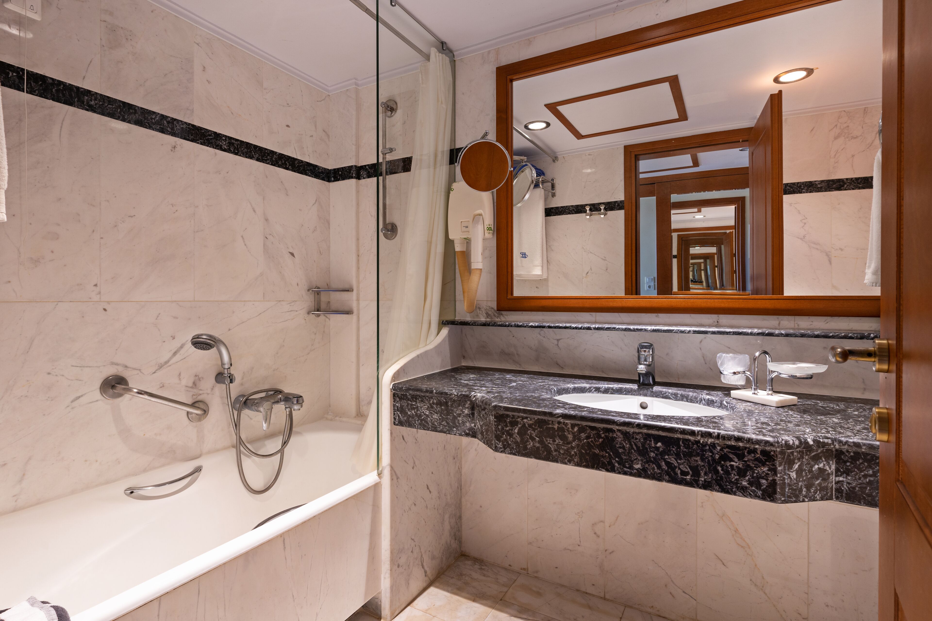 A modern bathroom with a glass-enclosed shower, a marble-tiled wall, a sink with a marble countertop, and a large mirror with a wooden frame.
