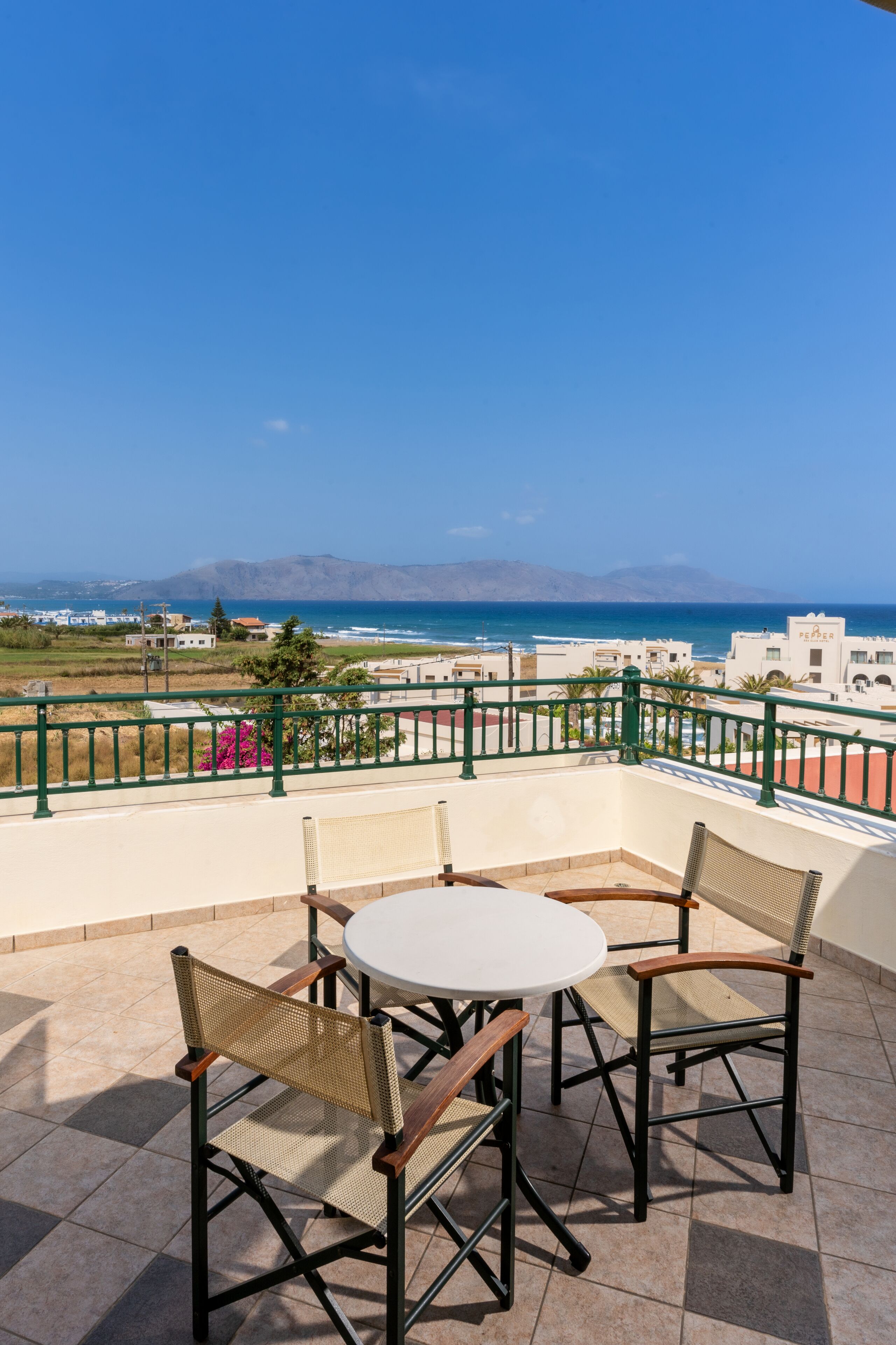 A terrace with a table and chairs, overlooking a coastal view with buildings and mountains in the distance.
