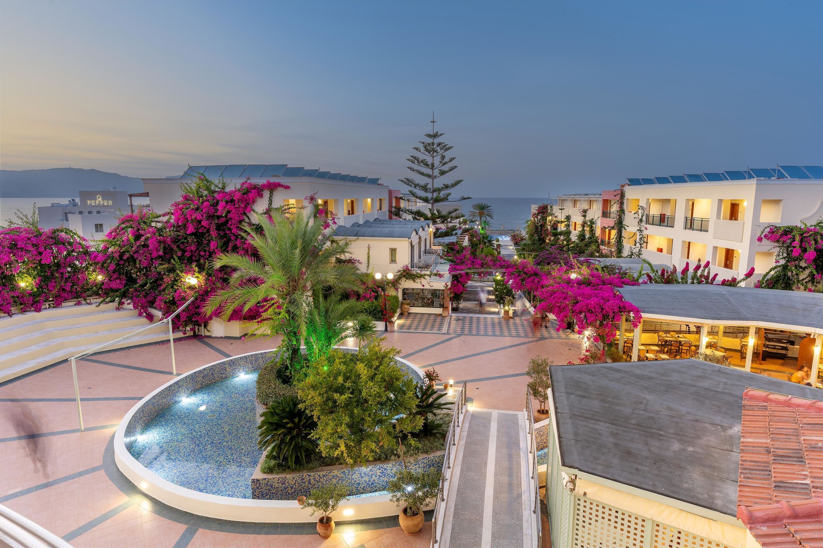 Un patio de hotel con piscina, rodeado de edificios con balcones y buganvillas rosadas.
