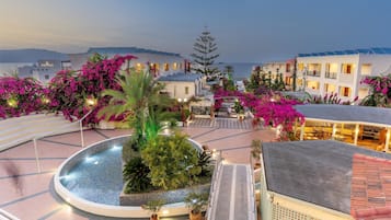 Un patio de hotel con piscina, rodeado de edificios con balcones y buganvillas rosadas.