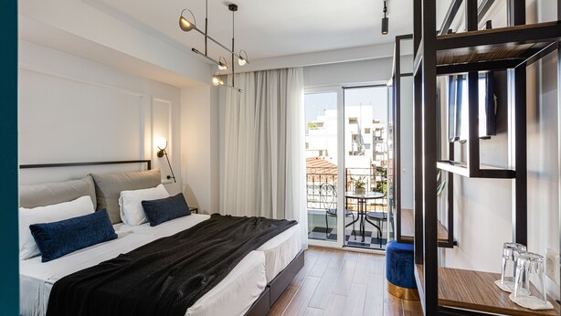 A modern hotel room with a large bed, a balcony with a table and chairs, and a view of the city. - Jo An Palace Hotel (Rethymno)