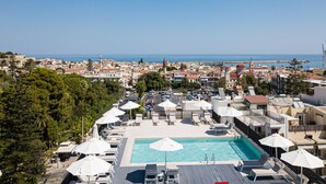 A rooftop pool area with lounge chairs and umbrellas, overlooking a coastal town with historic buildings and a clear blue sky. - Jo An Palace Hotel (Rethymno)