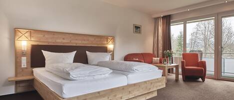 A hotel room with a large bed, a wooden headboard, a small table with a vase, and a red armchair.