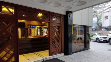 A building facade with a wooden lattice design, a visible entrance, and parked cars outside.