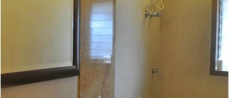 A bathroom with a shower, a toilet, and a window.
