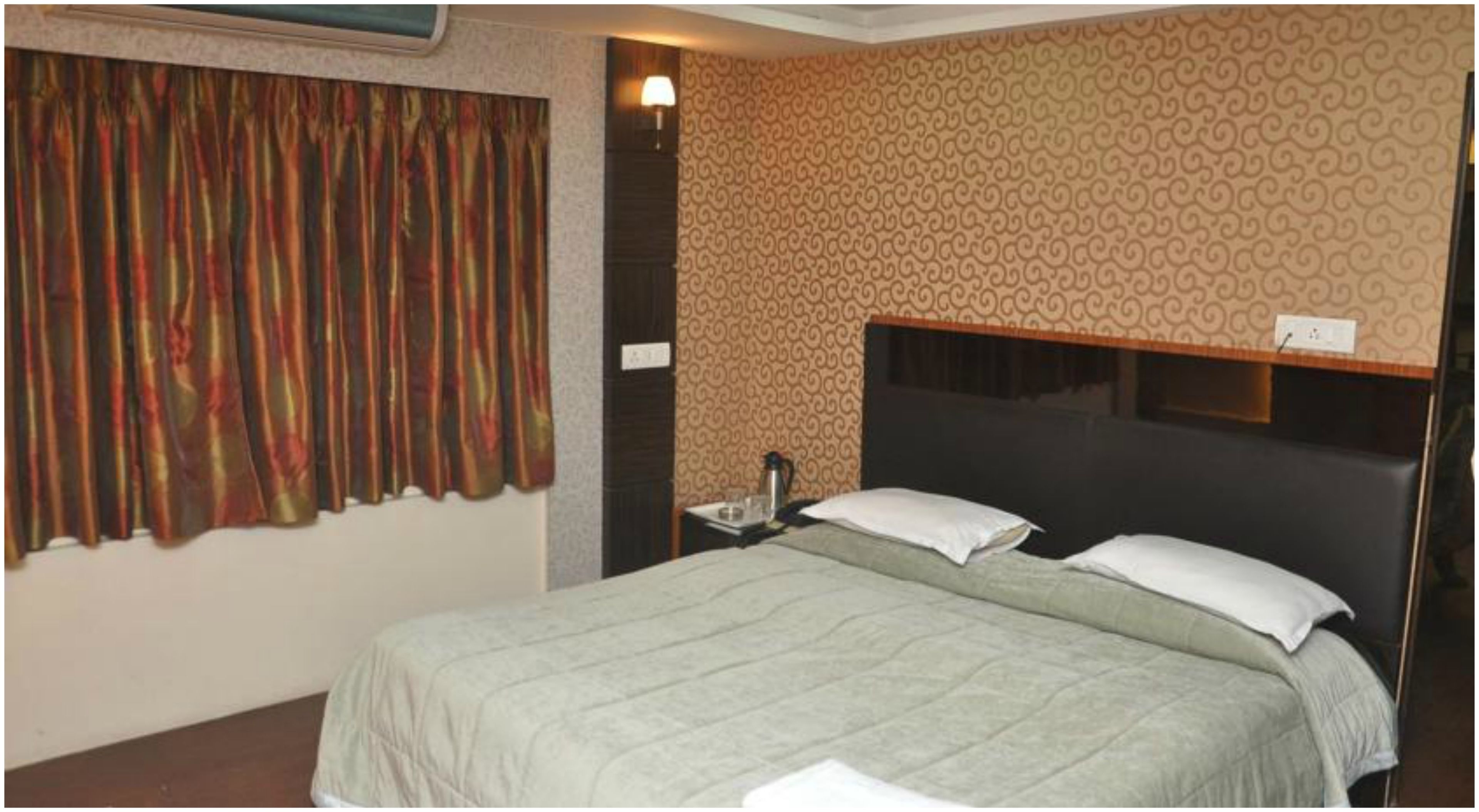 Une chambre d’hôtel avec un lit, une table de chevet, une lampe et un mur décoré d’un motif.