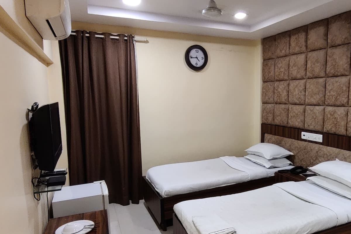 A hotel room with two single beds, a small desk with a chair, a television, and a clock on the wall.