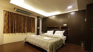 A modern hotel room with a large bed, wooden flooring, and a dark wood wardrobe. - Hotel Metro Palace (Mumbai)