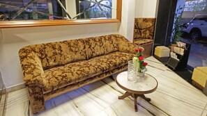 A sofa with a patterned fabric, a small round table with a clear glass, and a vase with red flowers. - Hotel Metro Palace (Mumbai)
