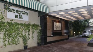 A hotel entrance with a sign in a foreign language, a covered walkway, and a parked car. - Hotel Metro Palace (Mumbai)