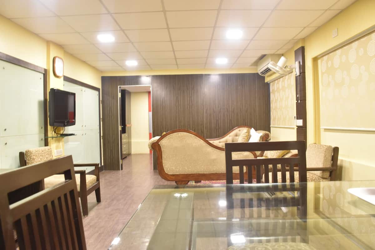 A hotel room with a glass table, wooden chairs, a sofa, and a television on the wall.