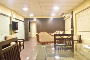 A hotel room with a glass table, wooden chairs, a sofa, and a television on the wall. - Hotel Metro Palace (Mumbai)