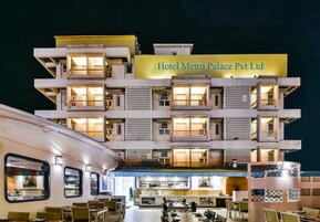 Un hotel de varios pisos con un letrero que dice "Hotel Metro Palace Pvt Ltd". Cuenta con un comedor con mesas y sillas, y un área de cocina visible.