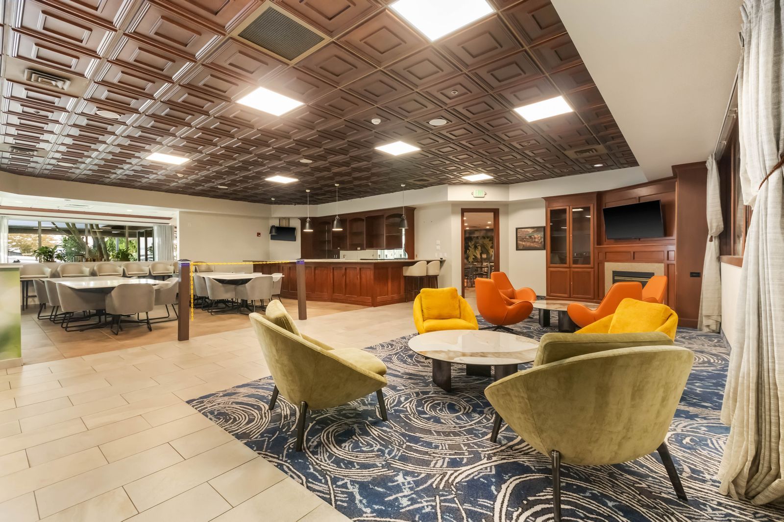 A hotel lobby with a dining area, a bar, and seating with a patterned carpet.