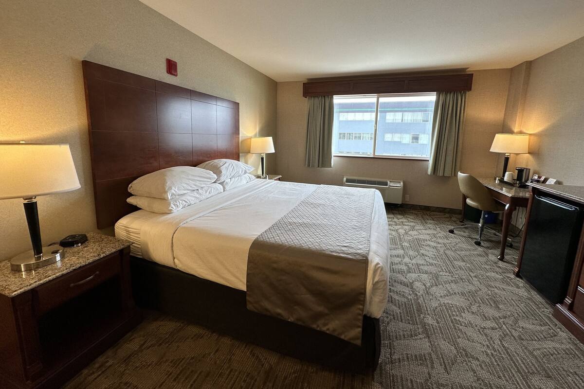 Habitación de hotel con una cama grande, dos mesitas de noche con lámparas, un escritorio con silla y una ventana con cortinas.