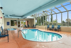 Une piscine intérieure avec des parois en verre transparent, un sol carrelé et plusieurs chaises longues.