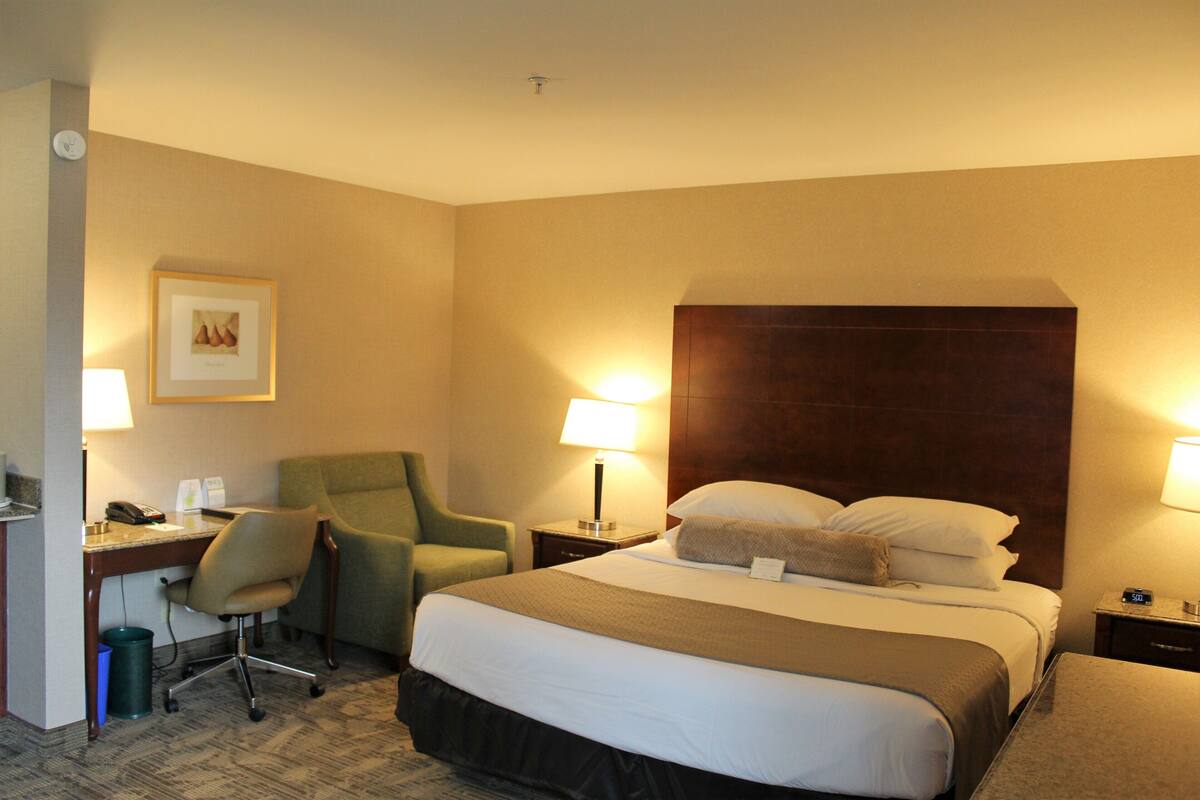 Una habitación de hotel con una cama grande, un escritorio con silla, un sillón verde y dos lámparas de noche.