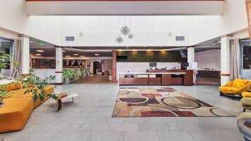 A spacious lobby with a reception desk, seating area, and a view of the kitchen in the background.
