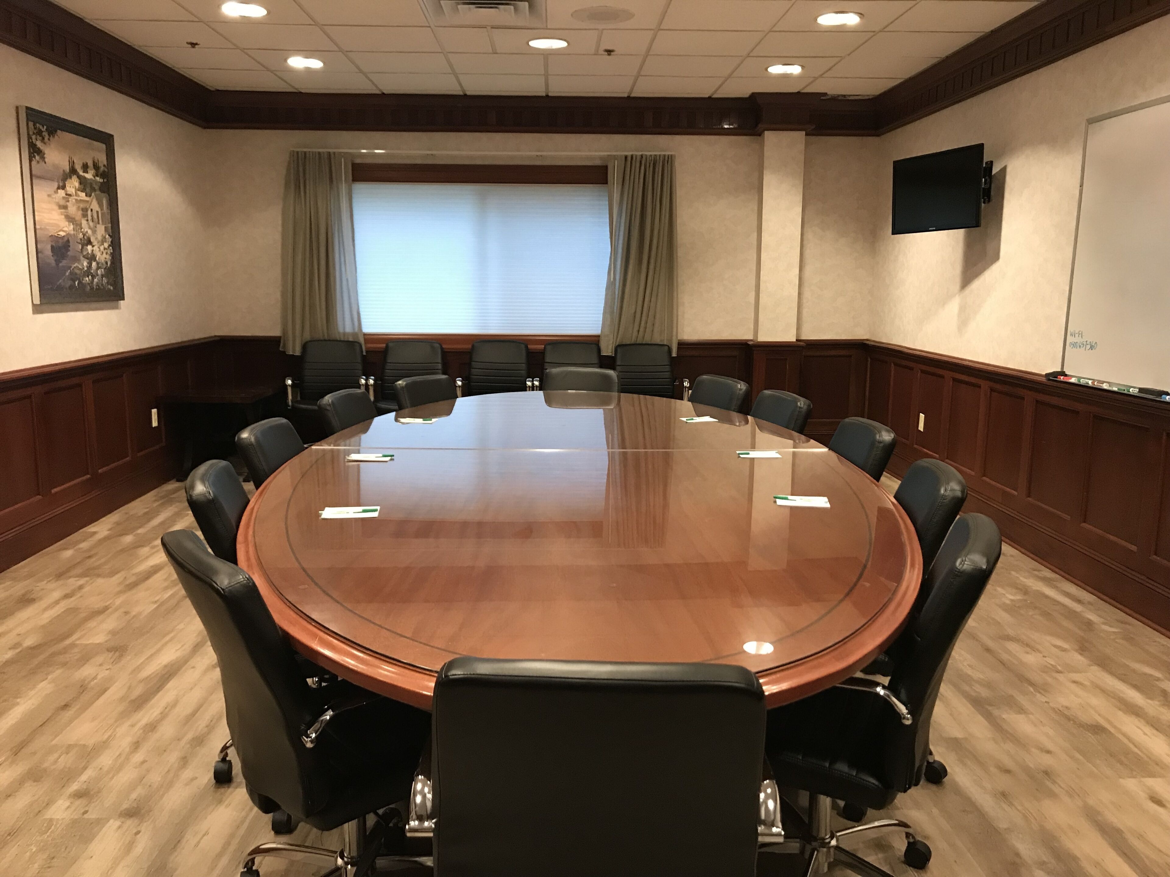 Une salle de conférence dotée d’une grande table ovale, de chaises en cuir noir, d’un tableau blanc et d’un téléviseur fixé au mur.