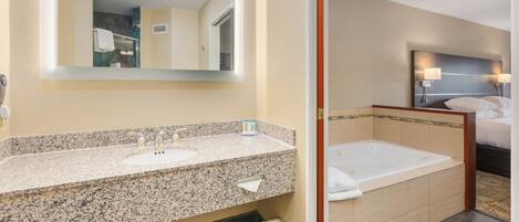 A hotel bathroom with a granite countertop sink, a large mirror, a bathtub, and a shower area.