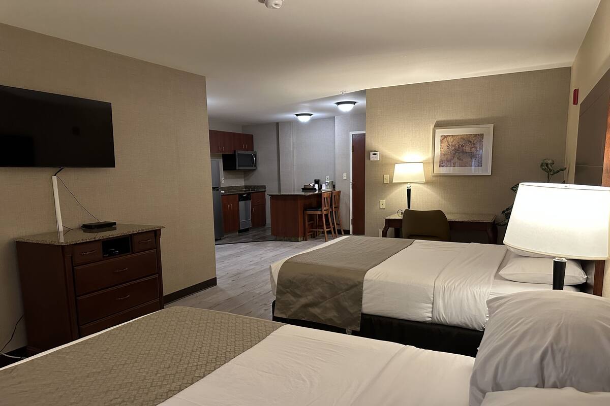 Habitación de hotel con dos camas, un escritorio, una silla, un televisor y una kitchenette al fondo.