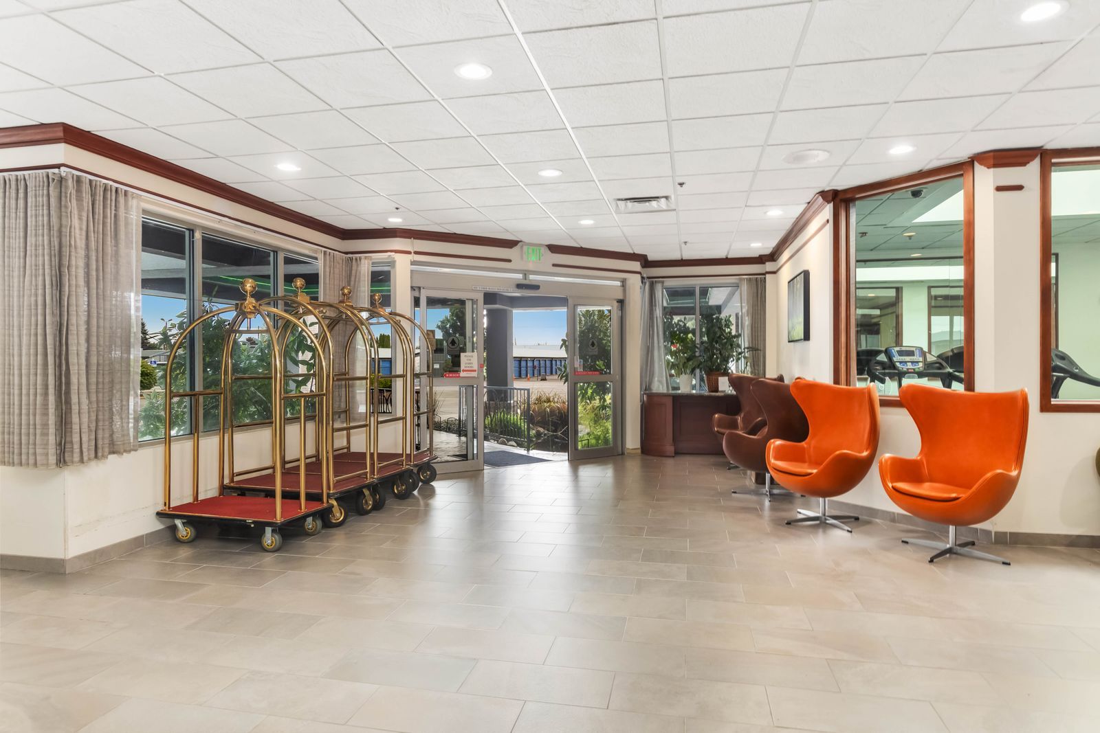 A hotel lobby with a reception desk, seating area with orange chairs, and a gold luggage cart.