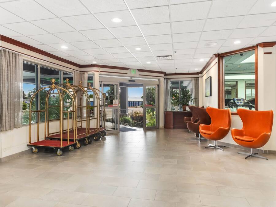 Eine Hotelhalle mit einer Rezeption, einer Sitzecke mit orangefarbenen Sesseln und einem goldenen Gepäckwagen.