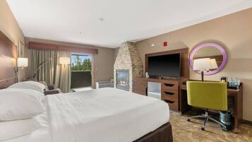 Habitació d'hotel amb un llit gran, televisió de pantalla plana, una llar de pedra, escriptori amb cadira i bany amb dutxa i vàter.