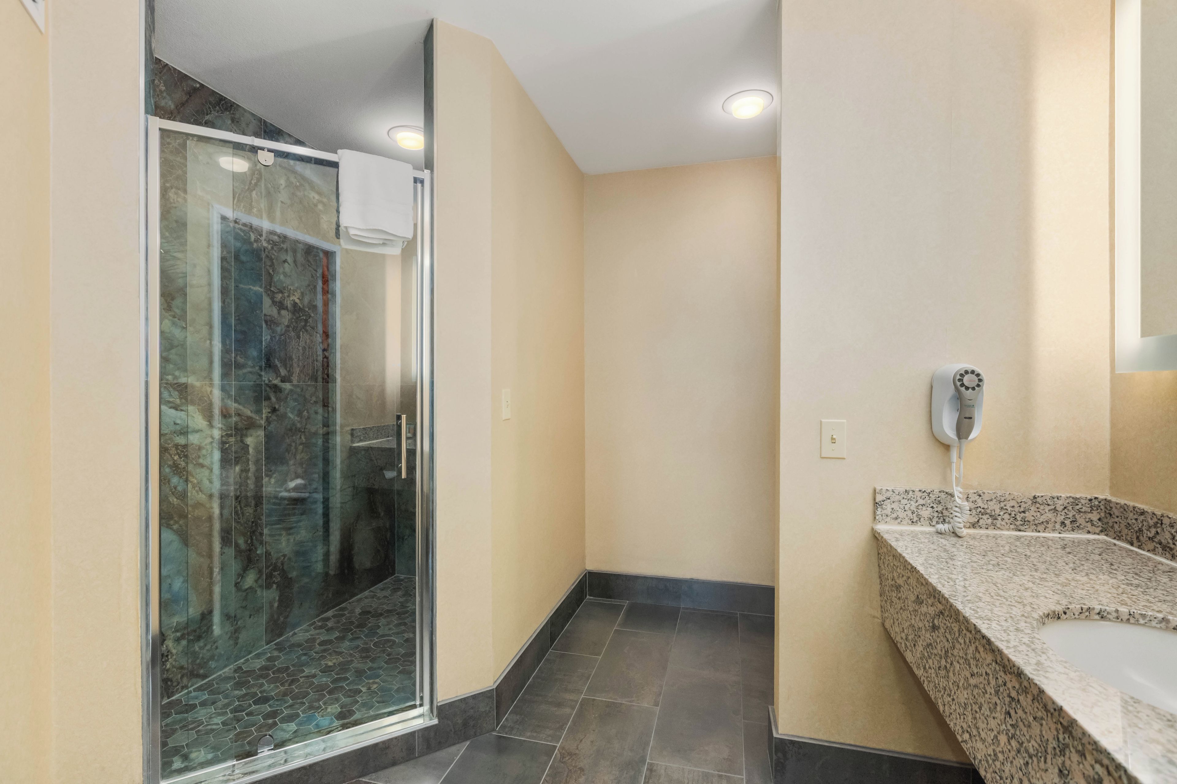 A modern bathroom with a glass shower enclosure, a granite countertop, and a built-in hairdryer.