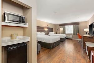 A hotel room with two beds, a desk, a television, a microwave, and a mini-fridge.