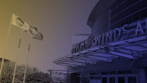 The exterior of the 'Winds of the Wind's Arena' building with a prominent sign and a flagpole with flags.
