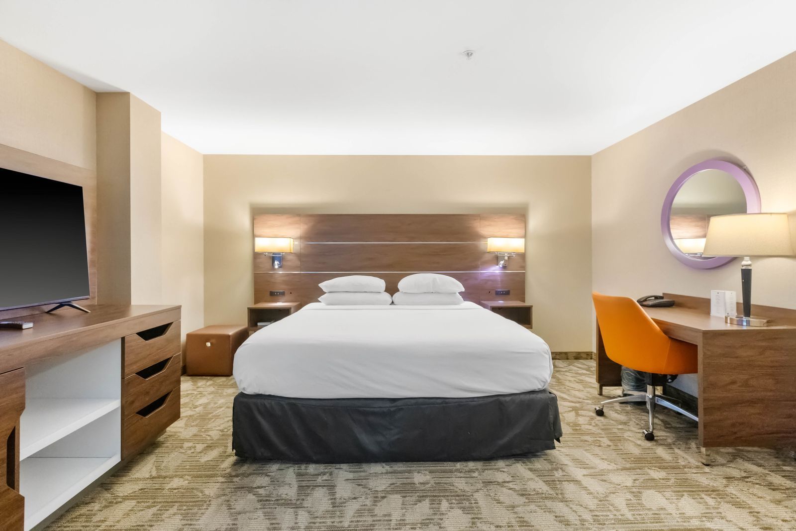 A hotel room with a bed, a desk, a chair, a television, and a mirror.
