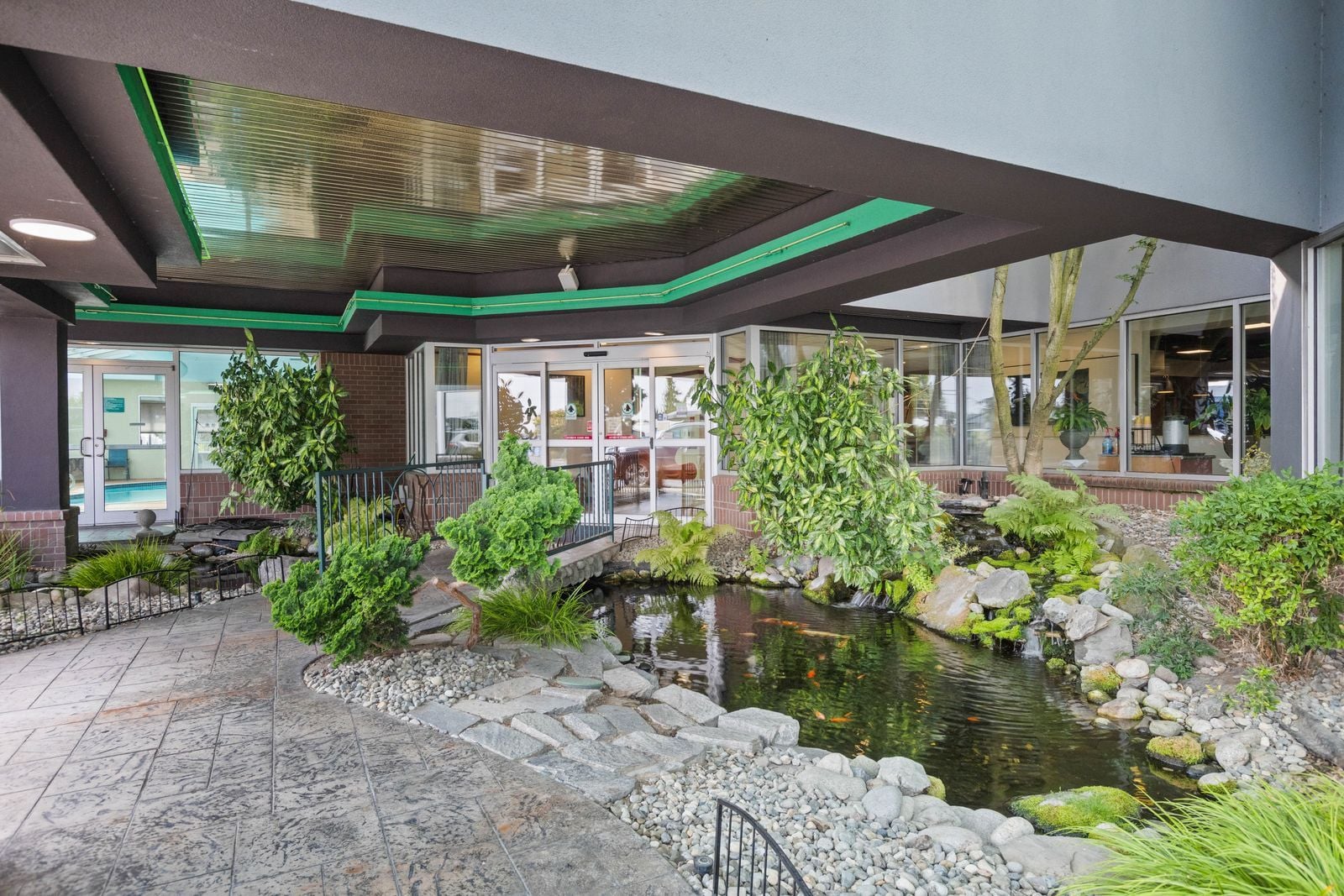 A hotel lobby with a koi pond, indoor plants, and a glass door entrance.