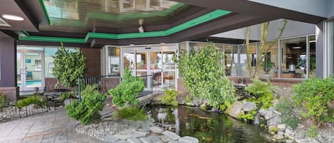A hotel lobby with a koi pond, indoor plants, and a glass door entrance.