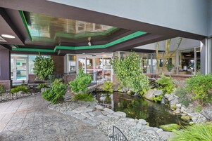 Un vestíbulo de hotel con un estanque de peces koi, plantas de interior y una entrada con puerta de cristal.
