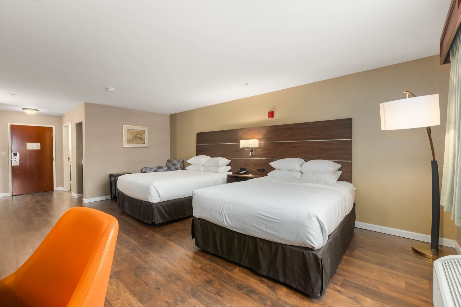A hotel room with two beds, a desk, a chair, and a lamp.