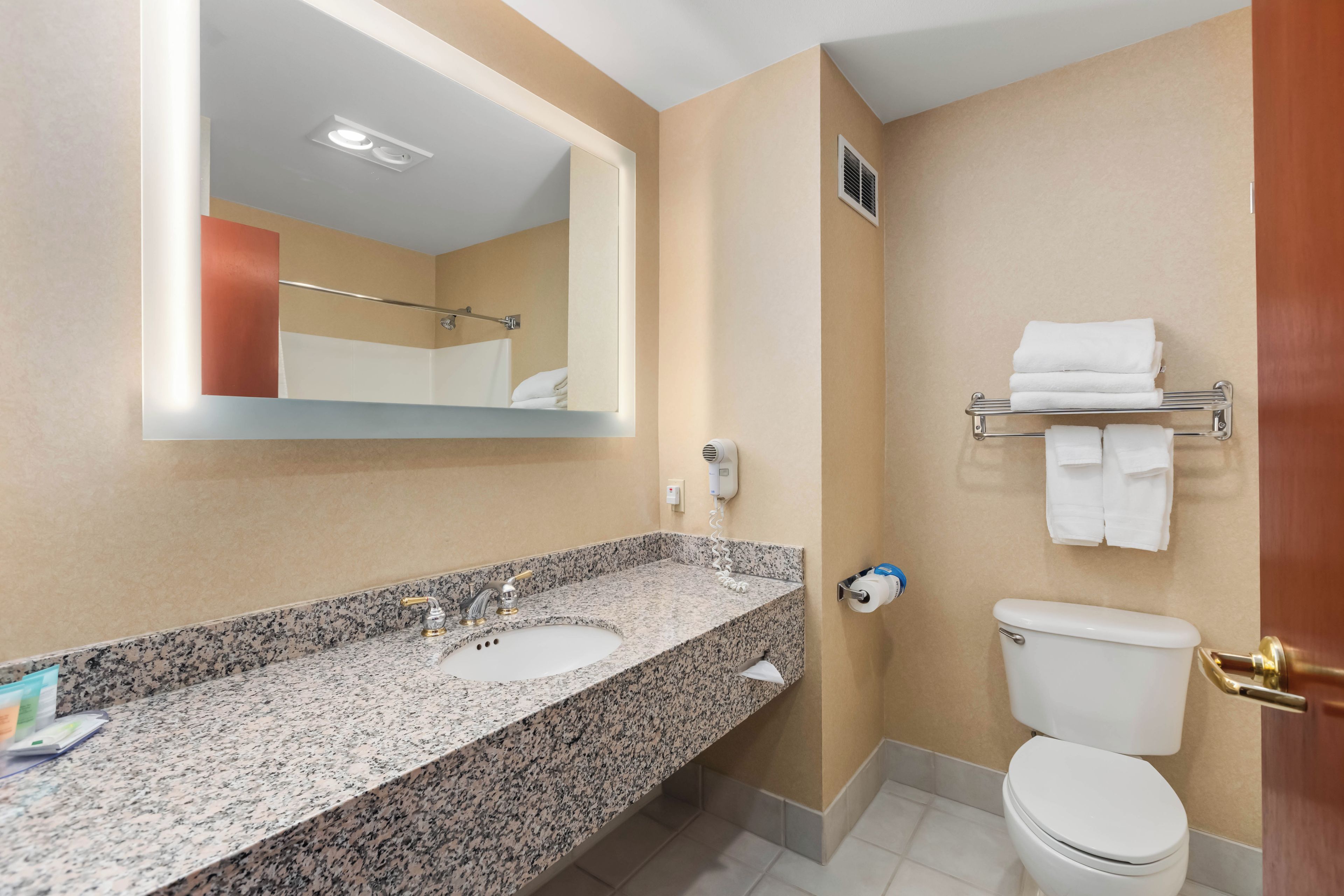 A bathroom with a granite countertop, a white sink, a toilet, and a towel rack.