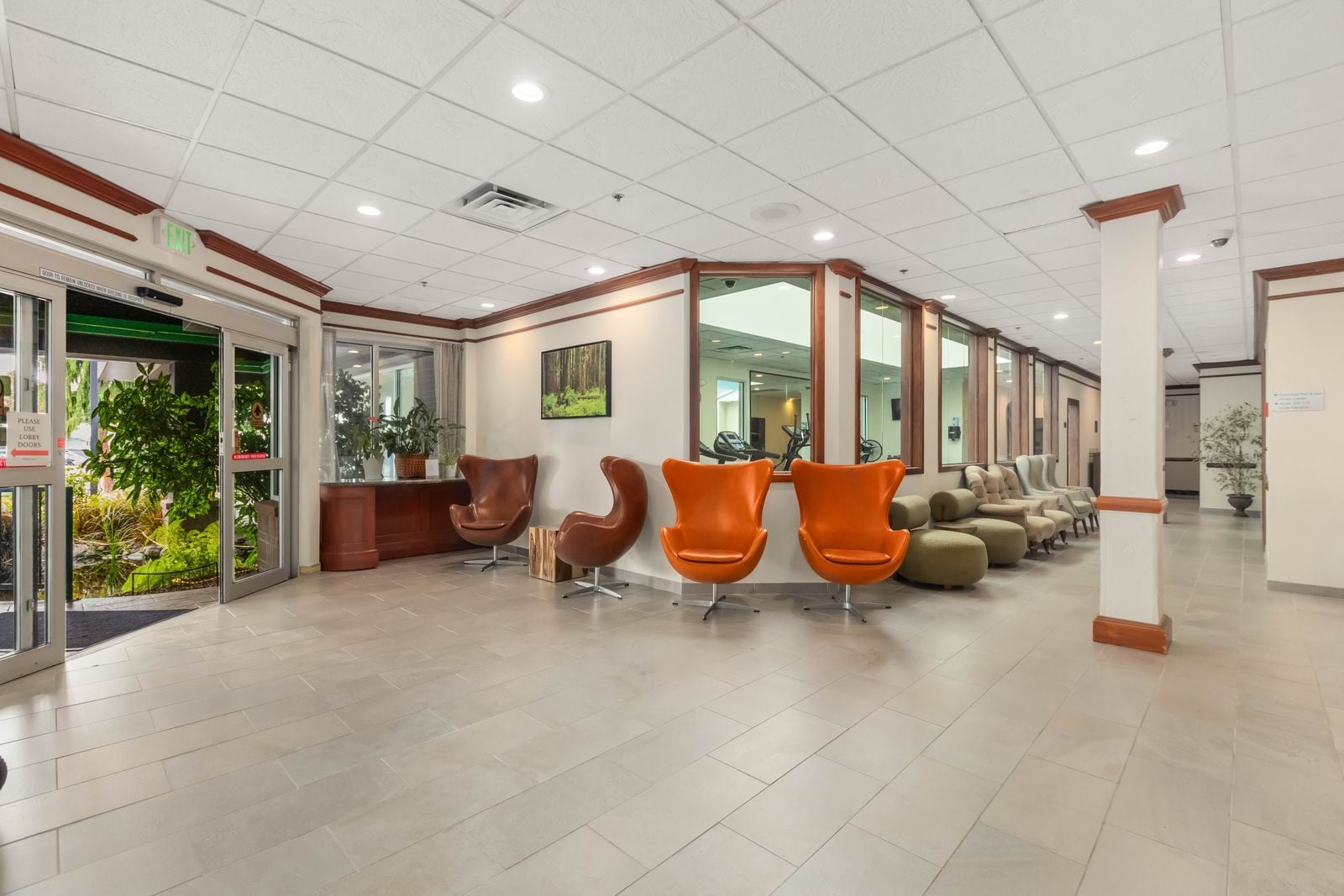 A lobby with a reception desk, two brown chairs, two orange chairs, a sofa, and a large mirror.