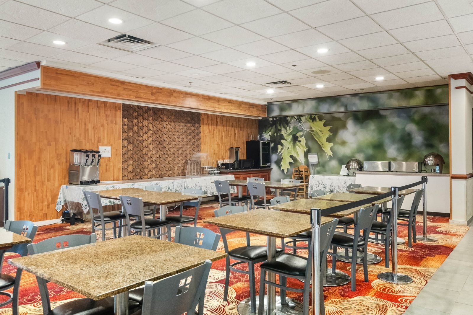 A hotel dining area with multiple tables and chairs, a coffee machine, and a kitchen area.